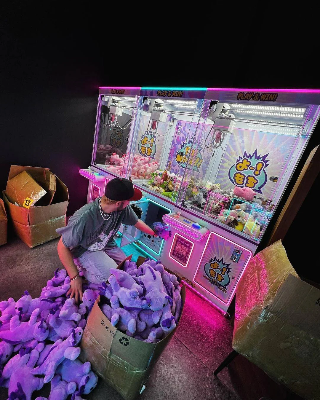 Claw machine filled with plush toys and a worker organizing them