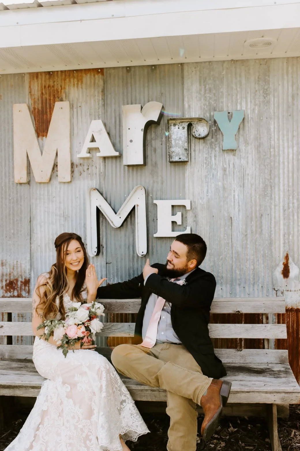 Couple celebrating engagement with playful pose in front of 'Marry Me' sign