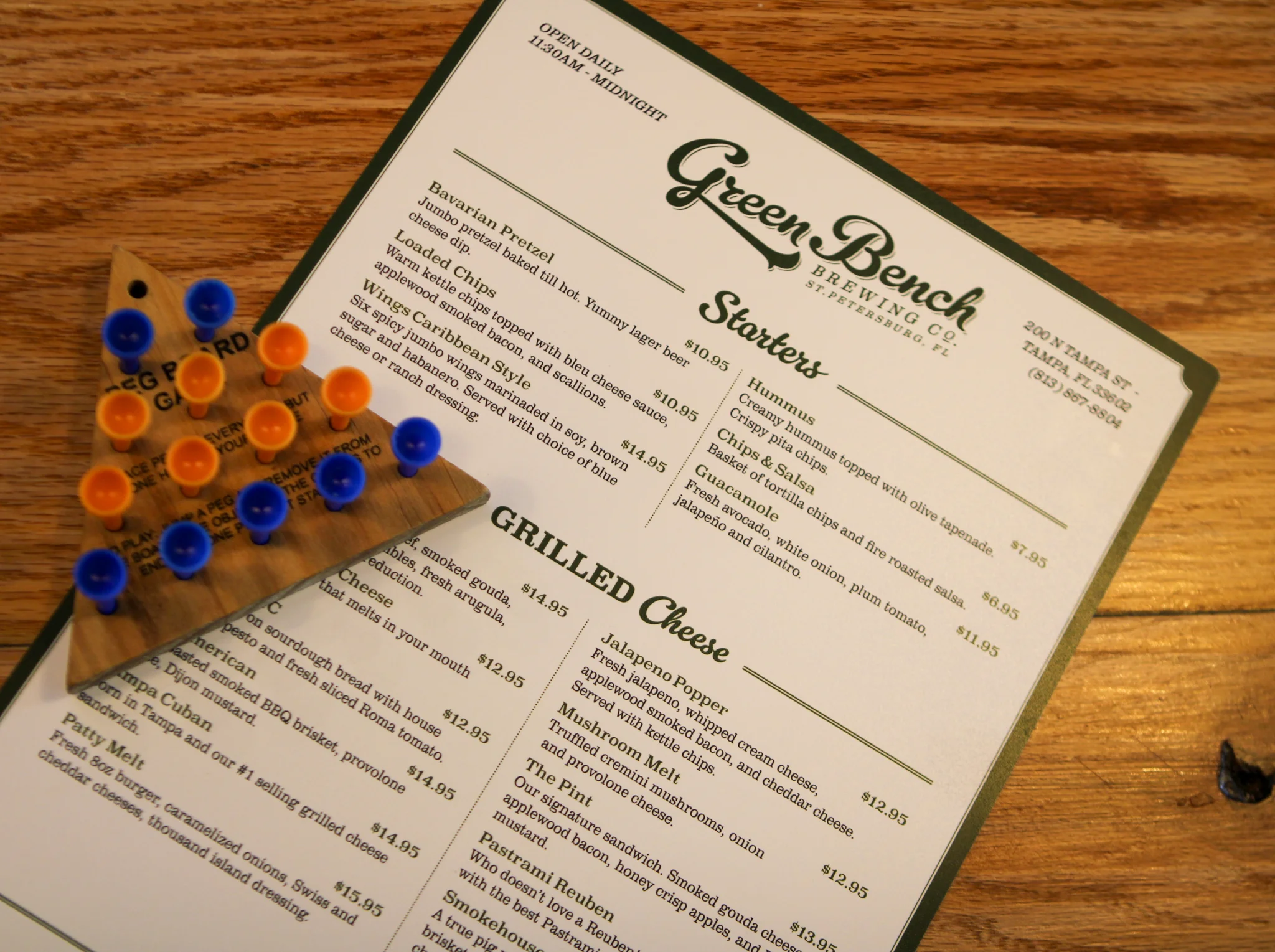 A menu featuring starters and grilled cheese options at a local brewery, accompanied by a triangular peg game.