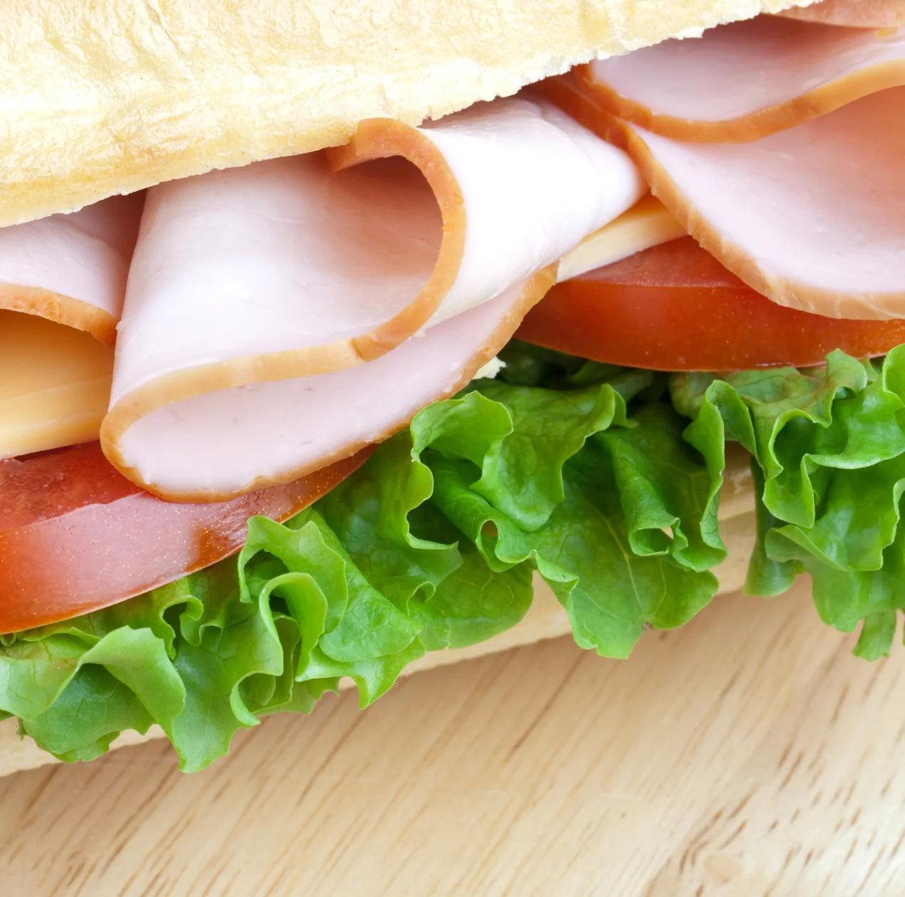 Close-up of a fresh turkey sandwich with sliced deli turkey, cheddar cheese, tomato, and leafy green lettuce on a toasted hoagie roll.