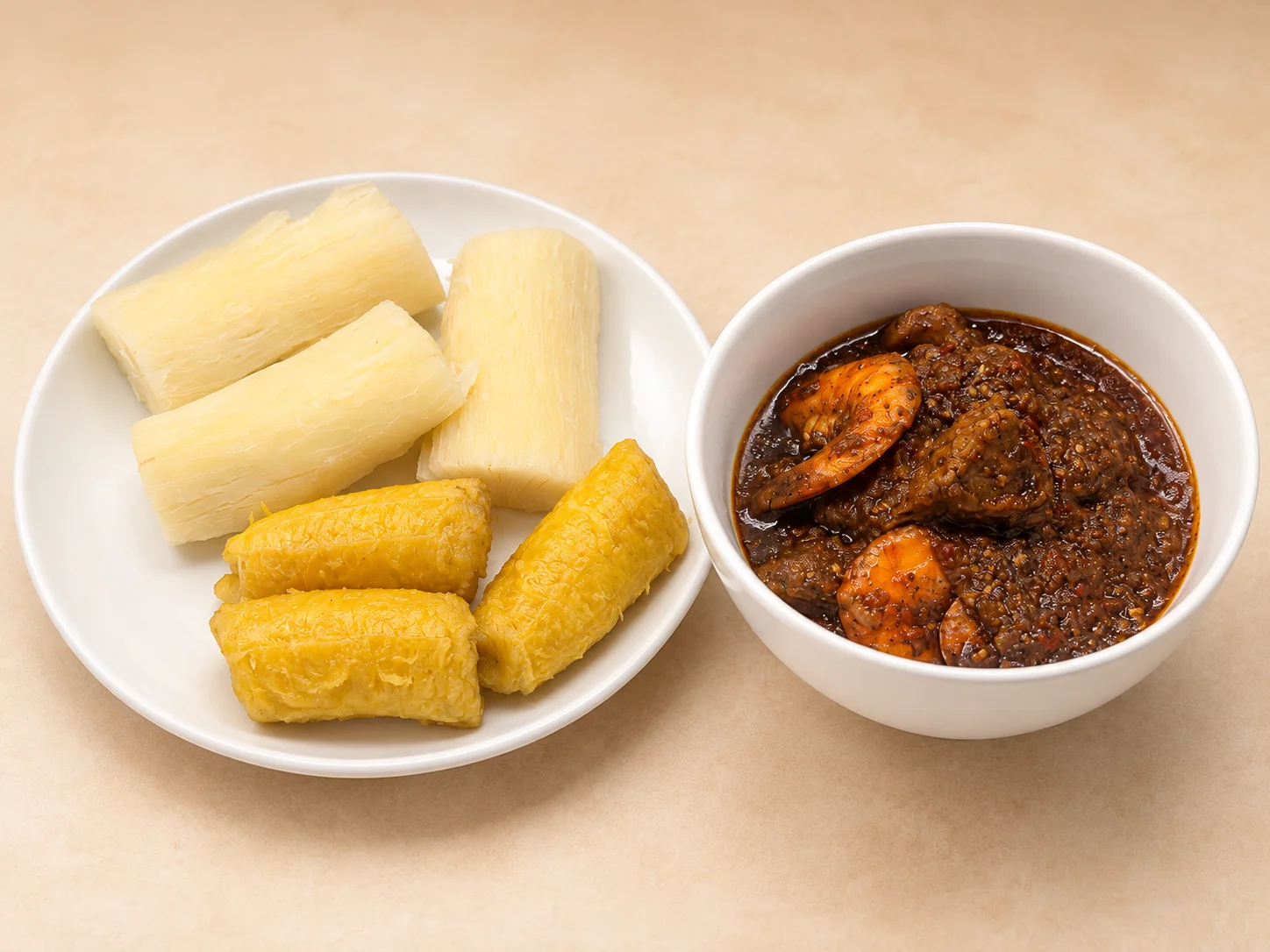 A plate of boiled cassava, including both yellow and white varieties, served with a bowl of spicy stew with shrimp.