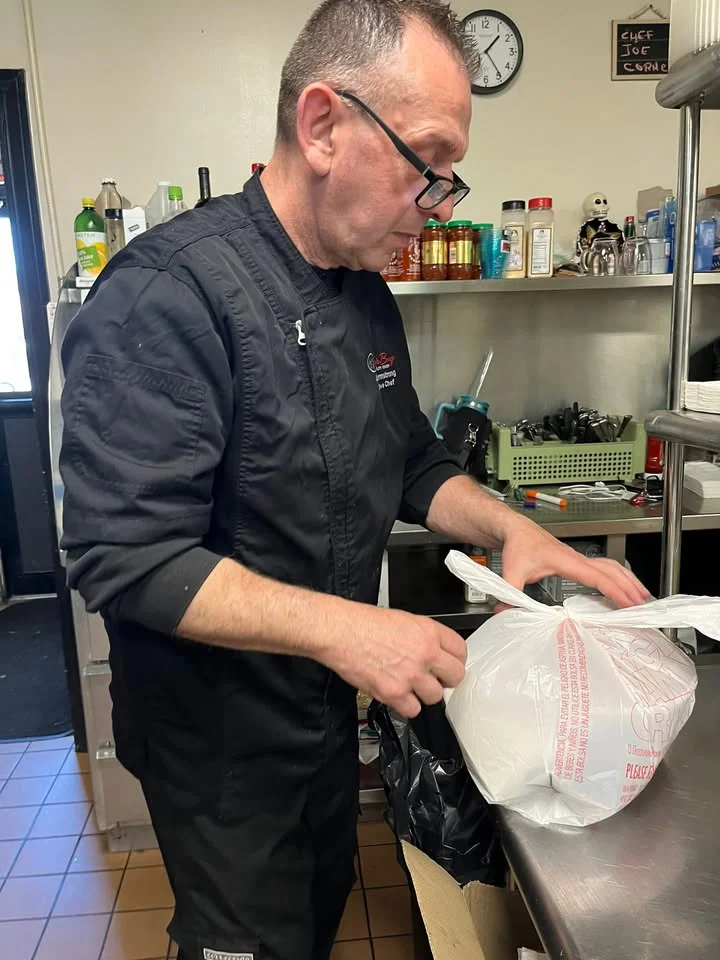 A chef in a black uniform is carefully packing a bag in a kitchen filled with various cooking supplies.