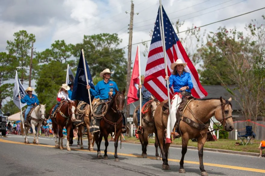 Cowboys riding horses in a parade holding flags
