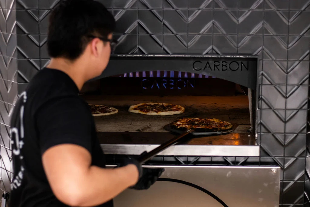 Chef retrieving Margherita pizza from a wood-fired oven