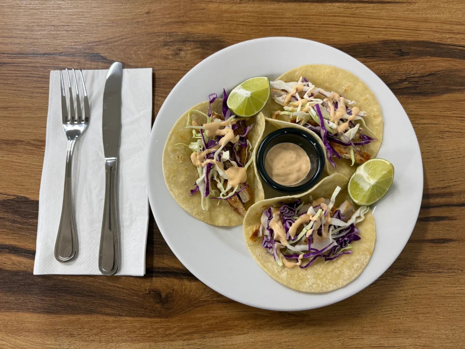 Three fish tacos with lime and sauce on a white plate
