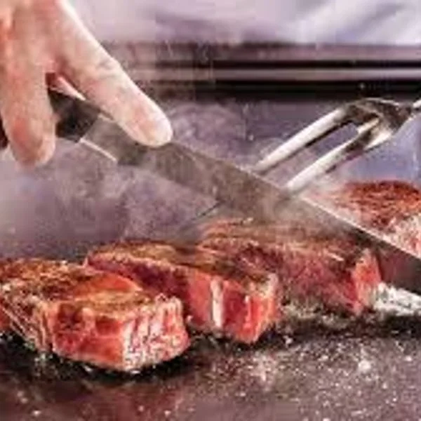 Sizzling steak being sliced on a grill, showcasing culinary expertise