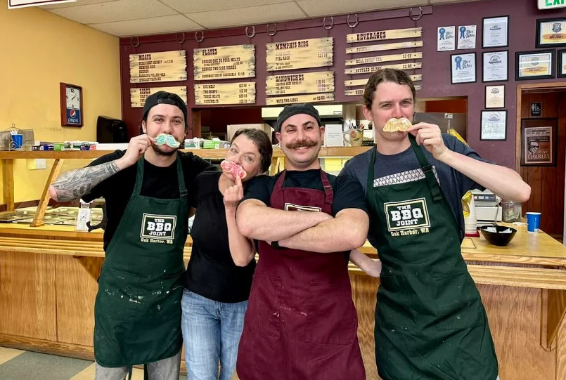 Fun staff posing with playful mustaches at a BBQ restaurant