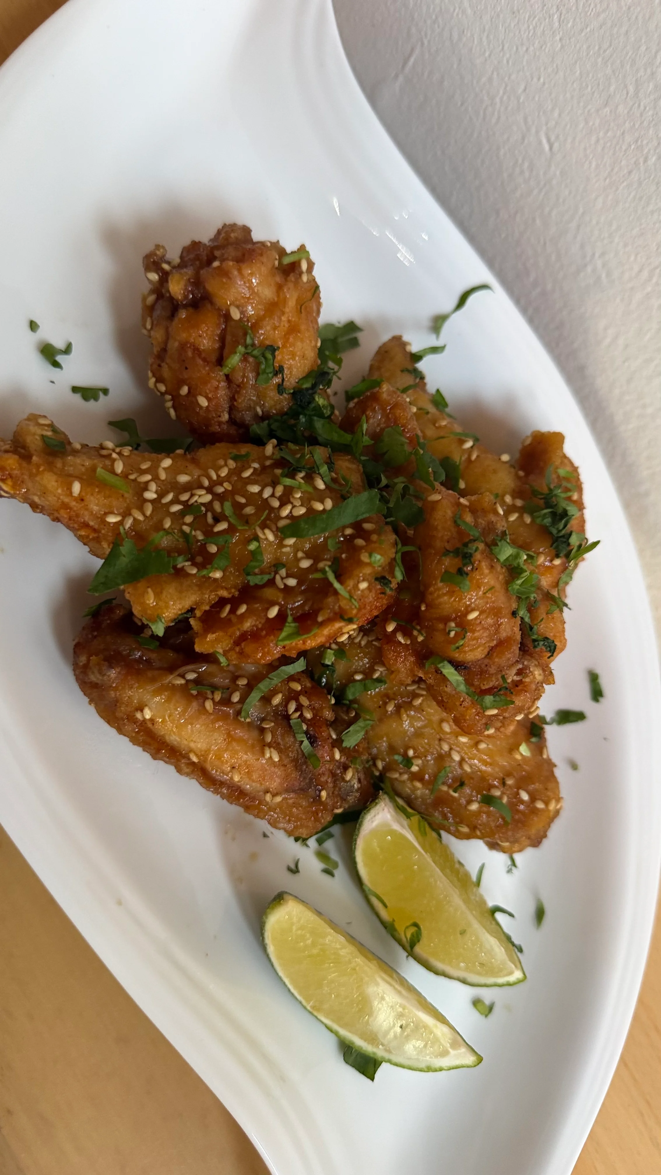 A plate of crispy chicken wings garnished with sesame seeds and cilantro, accompanied by fresh lime wedges.