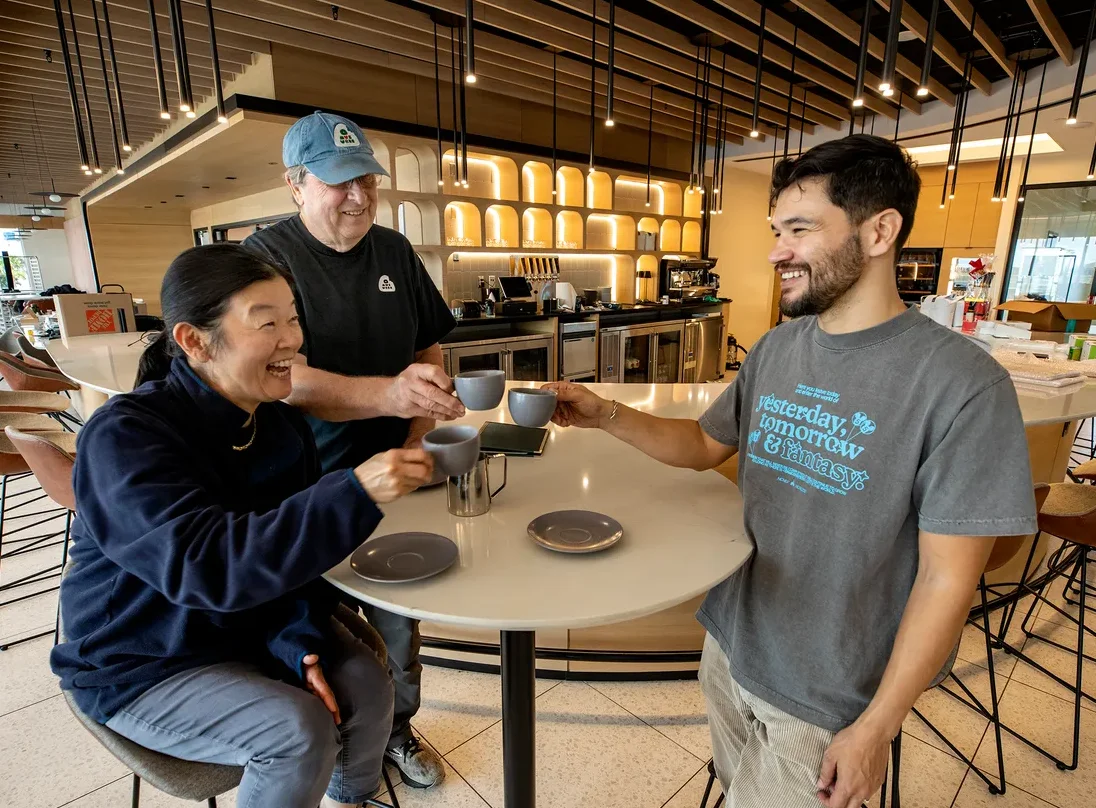 Three people toasting with coffee cups in a modern café setting