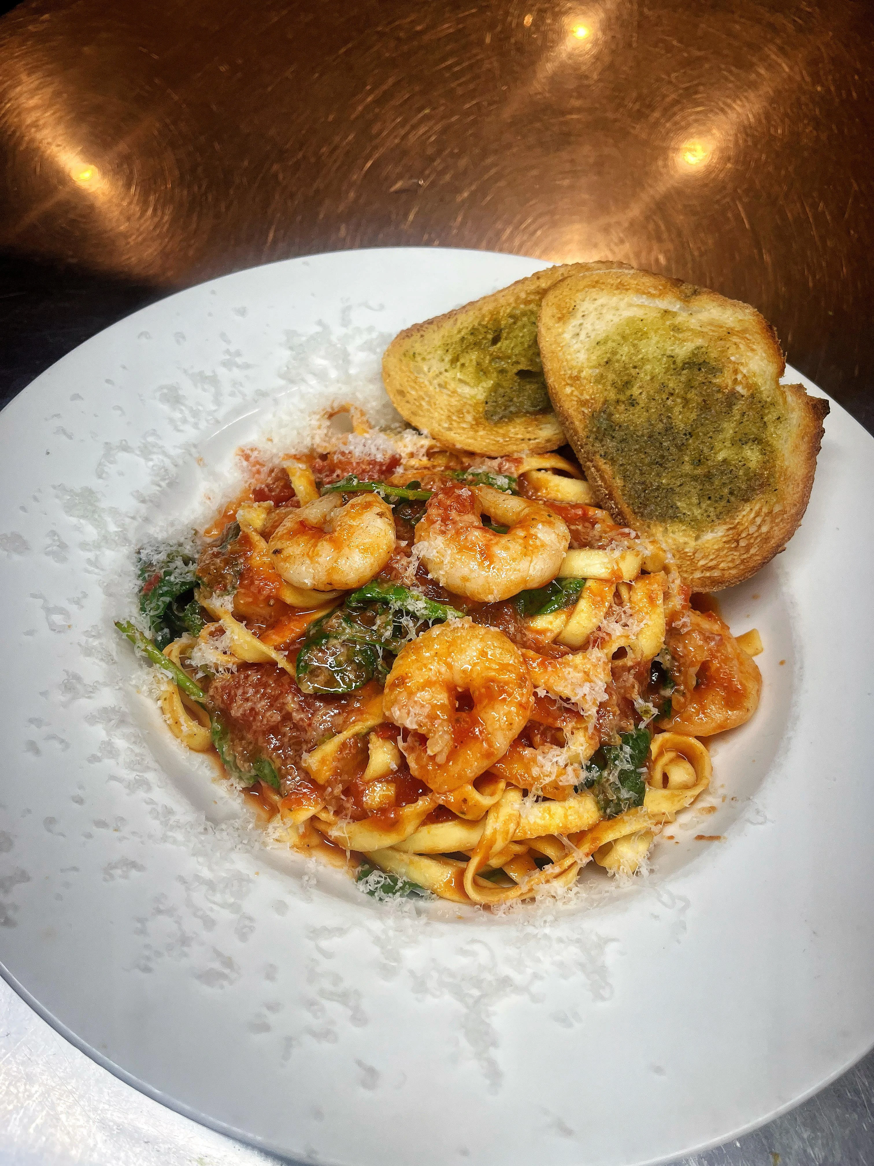 A plate of pasta topped with shrimp and greens in a savory sauce, served with two slices of toasted garlic bread.