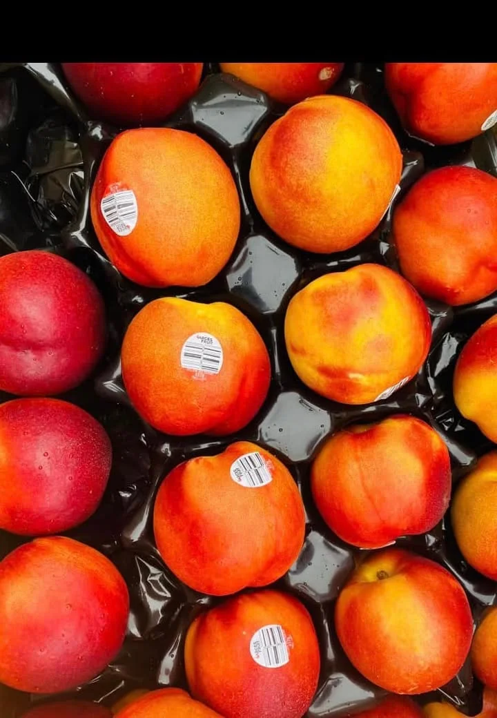 A variety of fresh peaches and nectarines with labels, arranged on a black surface.