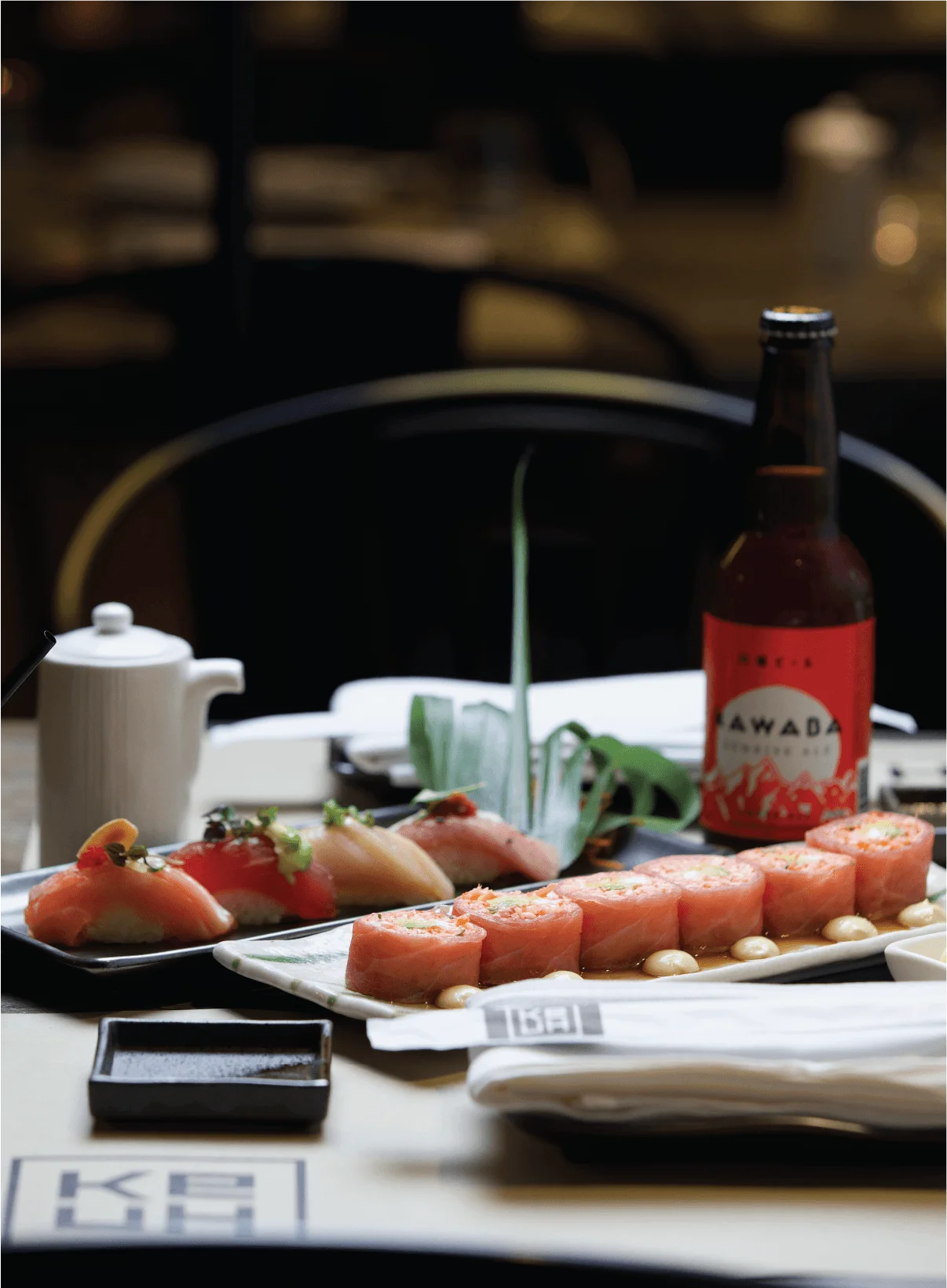 Seared salmon nigiri, grilled corn skewers, and a shrimp appetizer paired with a bottle and glass of red wine on a wooden table.