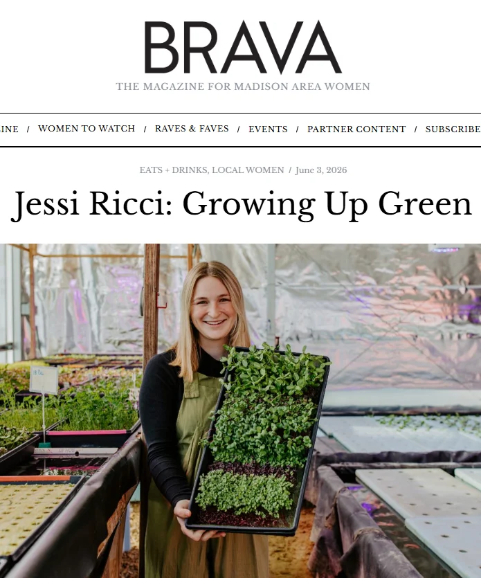 Woman holding a tray of microgreens in a greenhouse setting