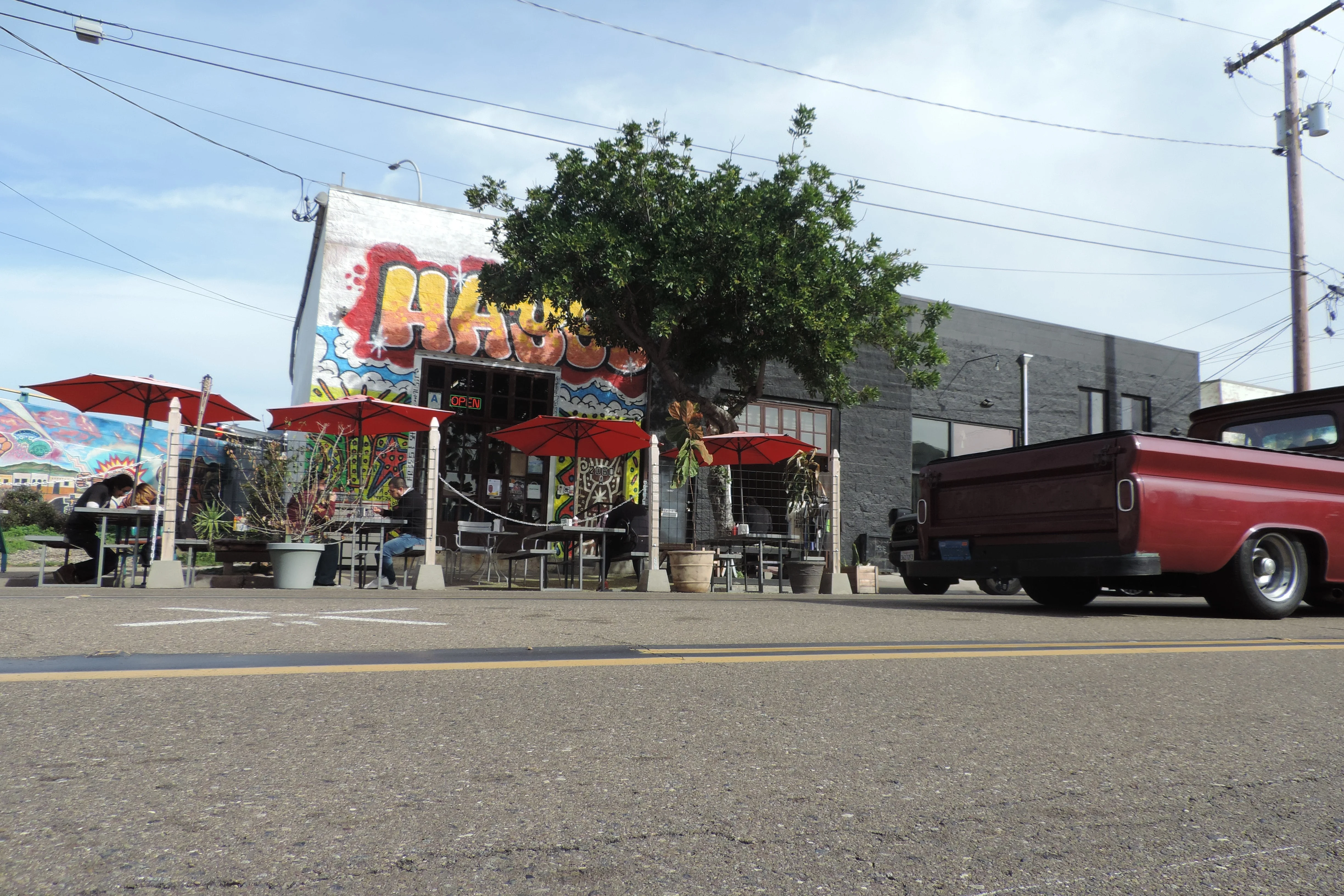 Hayes Burger's mural-covered storefront on Logan Ave in Barrio Logan, red umbrellas over the sidewalk patio