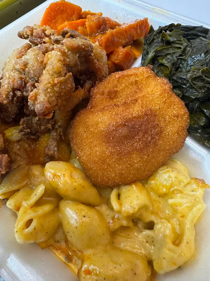 A hearty meal consisting of fried chicken, macaroni and cheese, collard greens, and sweet potatoes served on a plate.