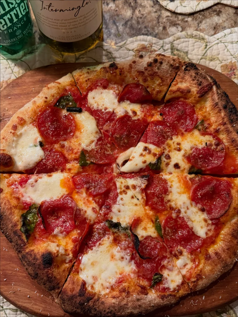 A large pizza with a crispy crust, topped with slices of pepperoni and melted cheese. It is placed on a wooden board, surrounded by beverage bottles.