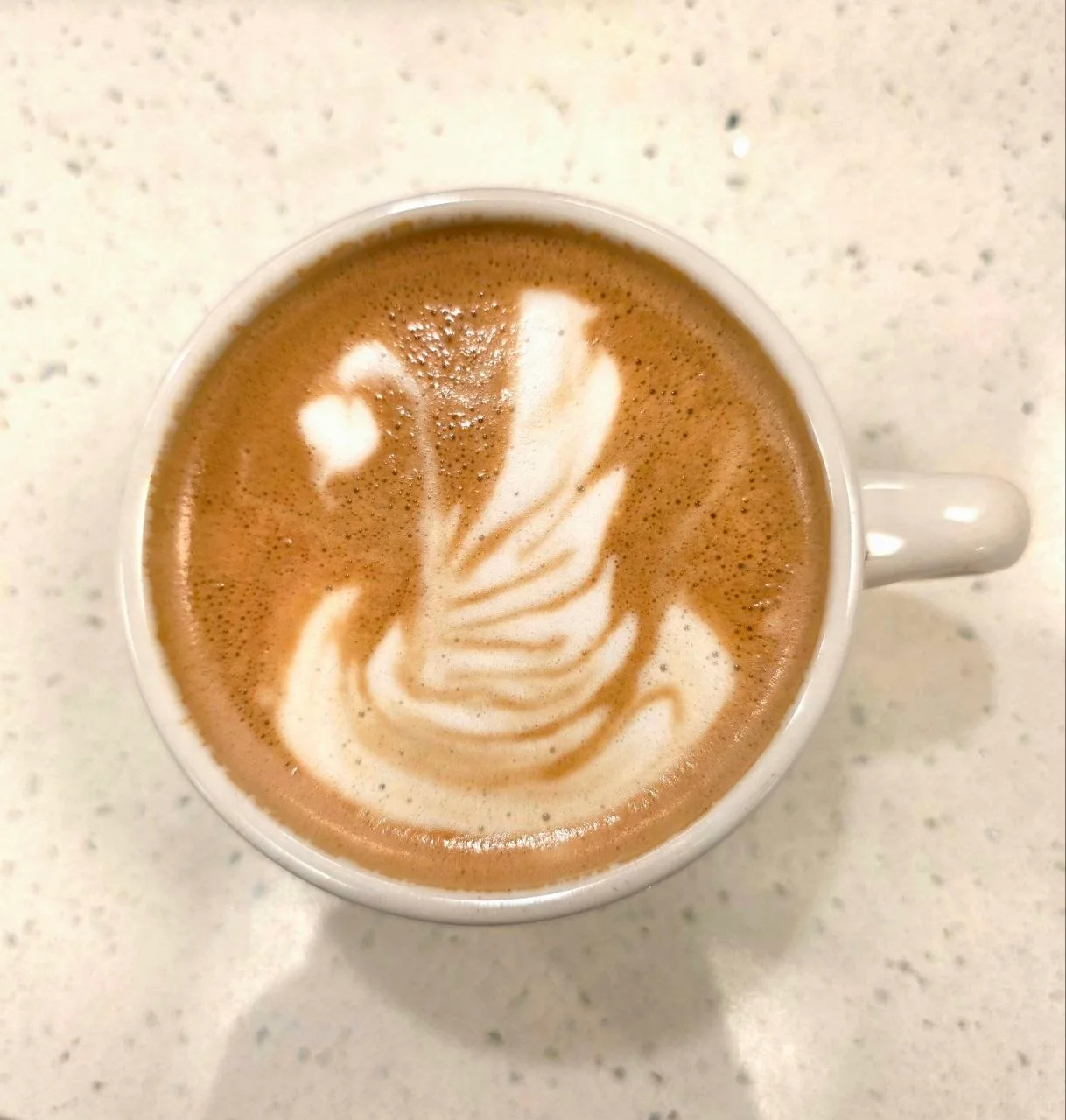 A beautifully crafted latte featuring intricate foam art resembling a swan, served in a white cup.