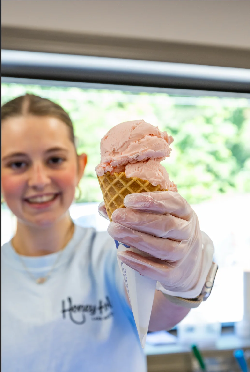 A smiling employee holding a cone of pink ice cream in a shop.