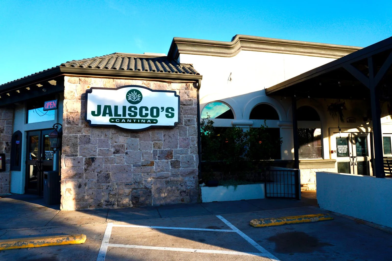 An exterior view of a restaurant with a stone facade and a visible sign indicating its name, complemented by clear blue skies.