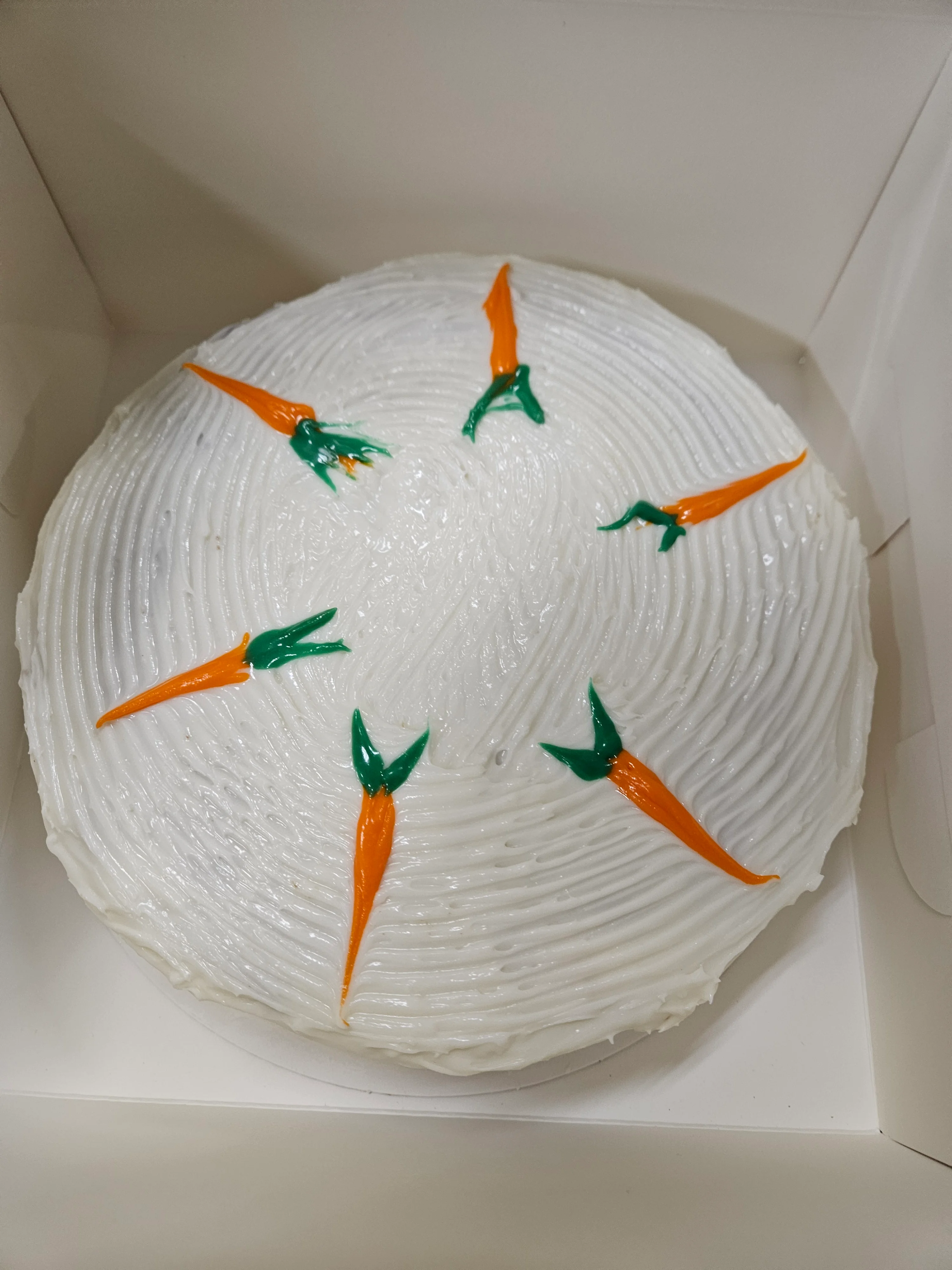 Carrot cake decorated with vibrant icing in a bakery box