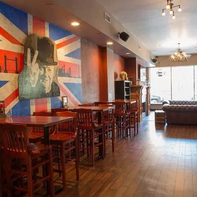 An interior view of a bar featuring wooden tables and chairs, with a mural of a historical figure against a Union Jack backdrop.