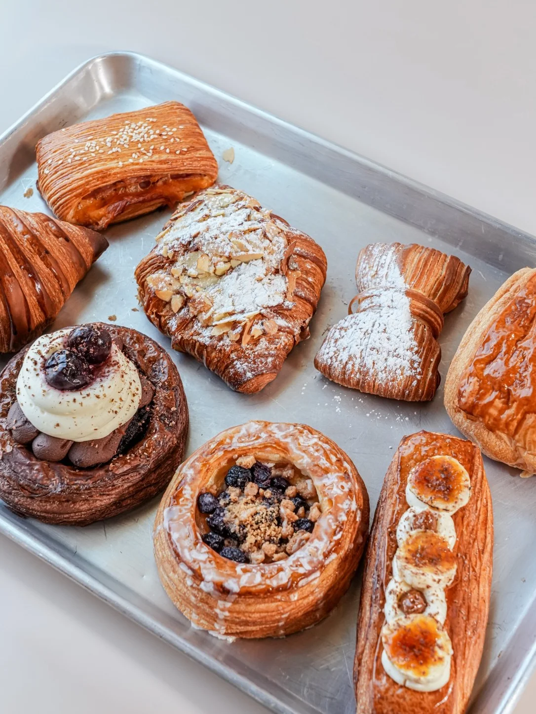 An assortment of pastries arranged on a metal tray, featuring croissants, fruit toppings, and garnishes of berries and mint.