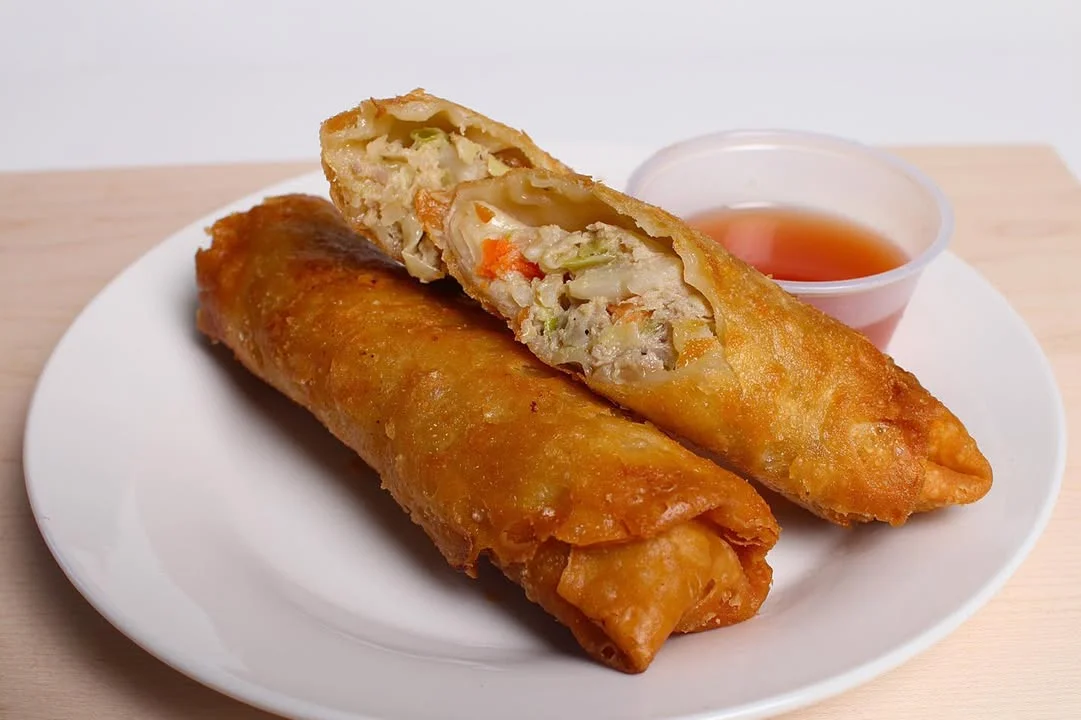 Two crispy spring rolls filled with vegetables, served with a side of dipping sauce.