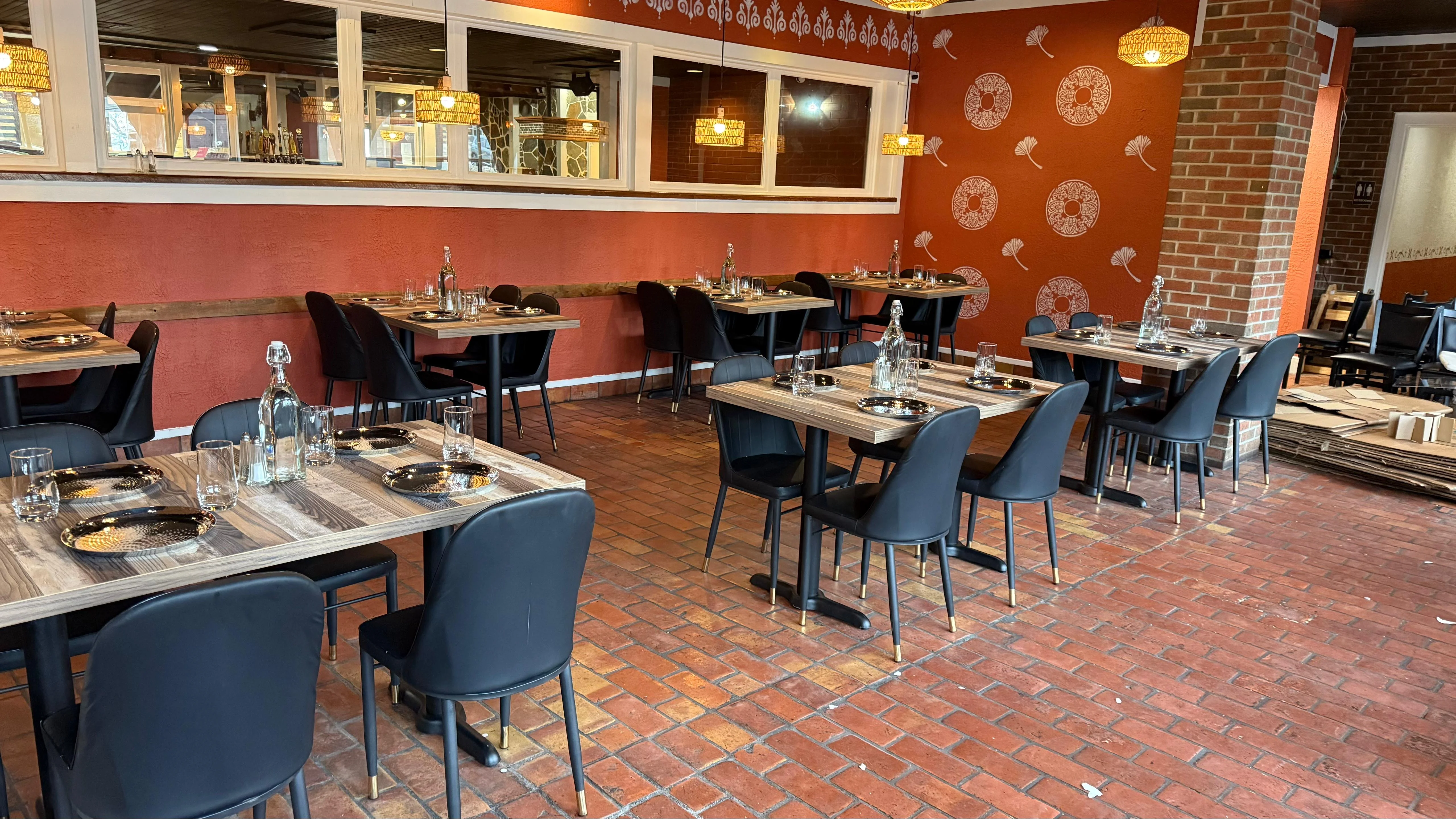 A charming restaurant interior showcasing a mix of tables and black chairs. The warm red walls are embellished with decorative designs and stylish light fixtures add character.