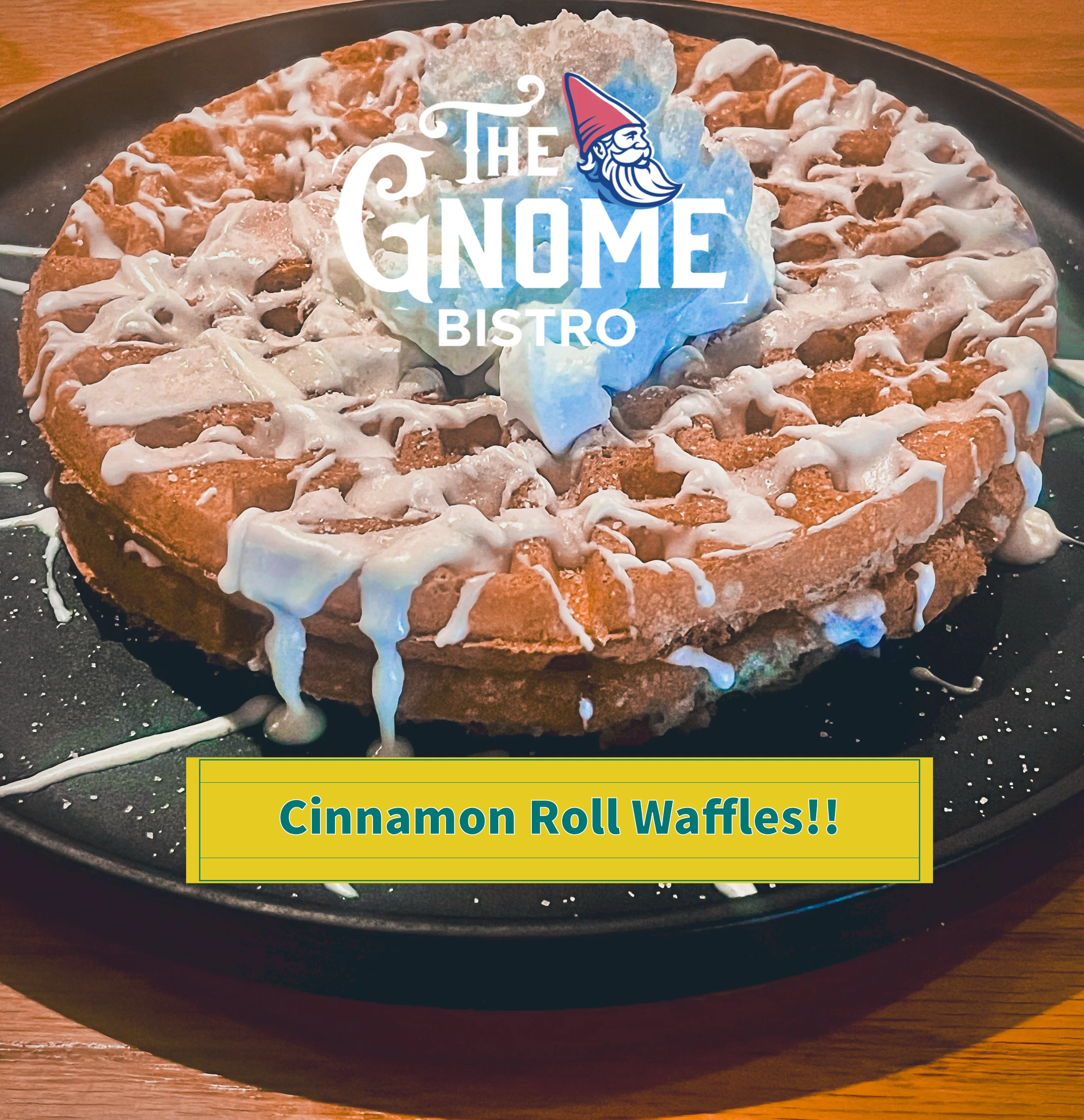 A close-up of cinnamon roll waffles drizzled with icing on a black plate.