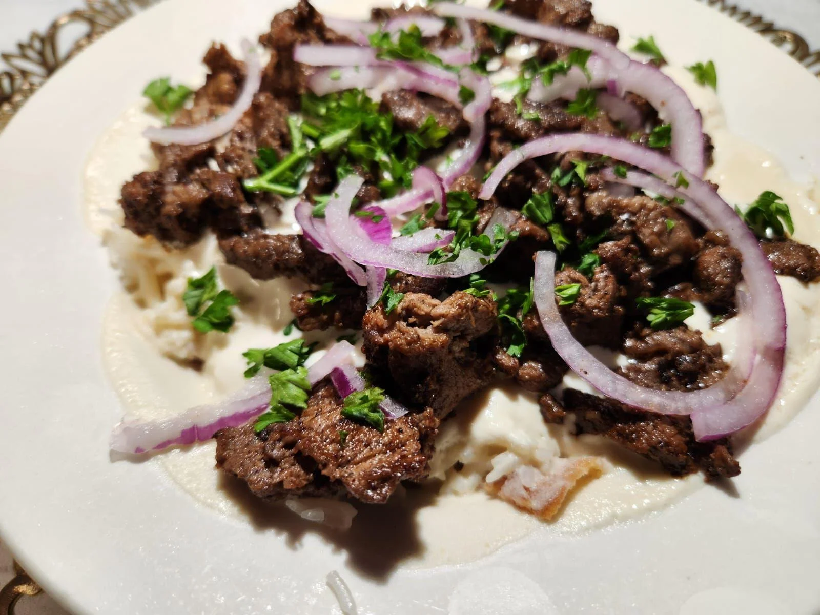 A plate of sautéed meat served over a bed of rice, garnished with onions and parsley.