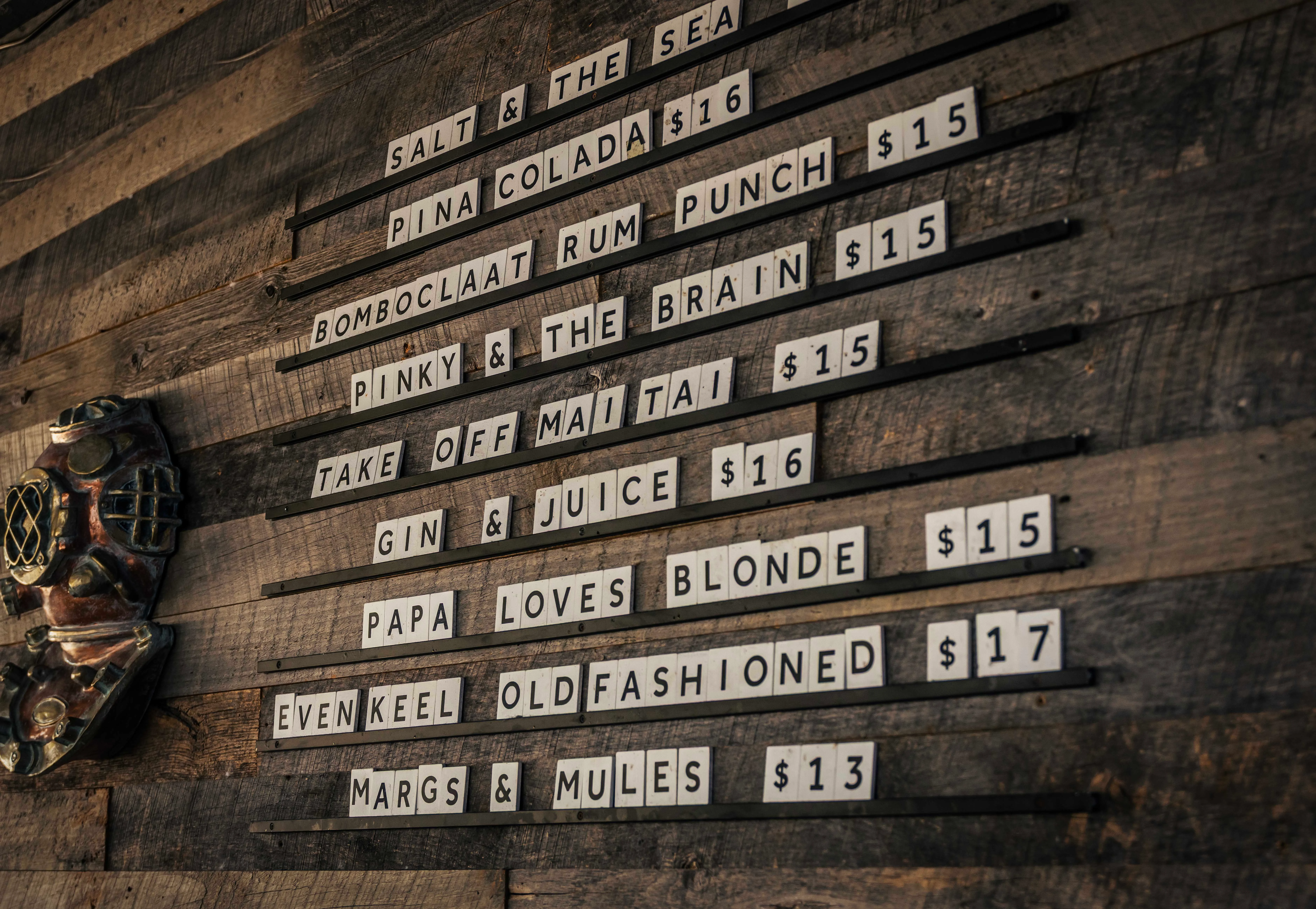 Menu board with cocktail names and prices on a wooden wall.