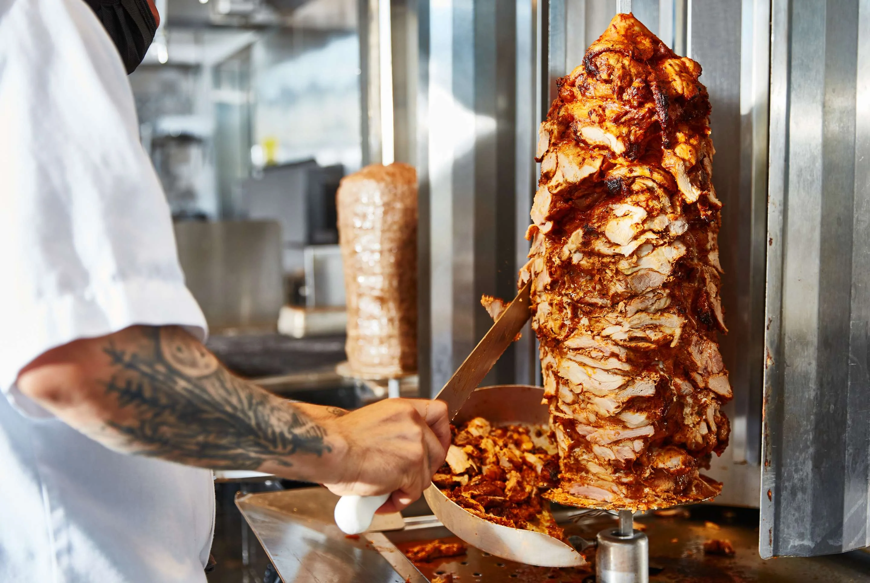 Chef slicing shawarma from a vertical rotisserie