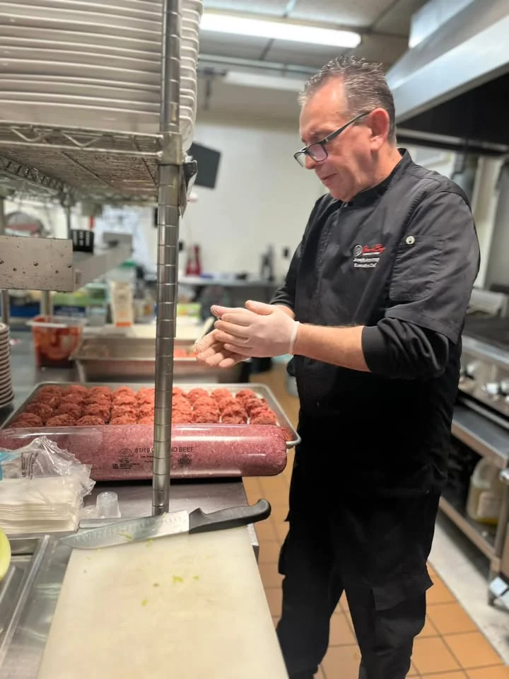 A chef preparing ground meat into patties in a restaurant kitchen. The chef is wearing gloves and concentrating on his task.