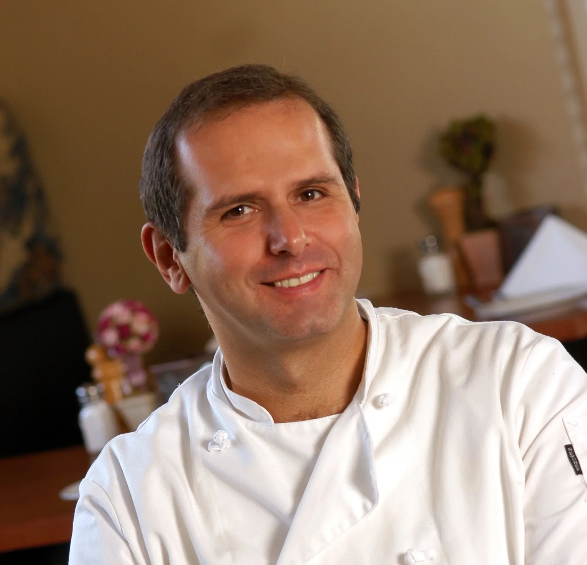 Chef in a white coat smiling in a restaurant setting