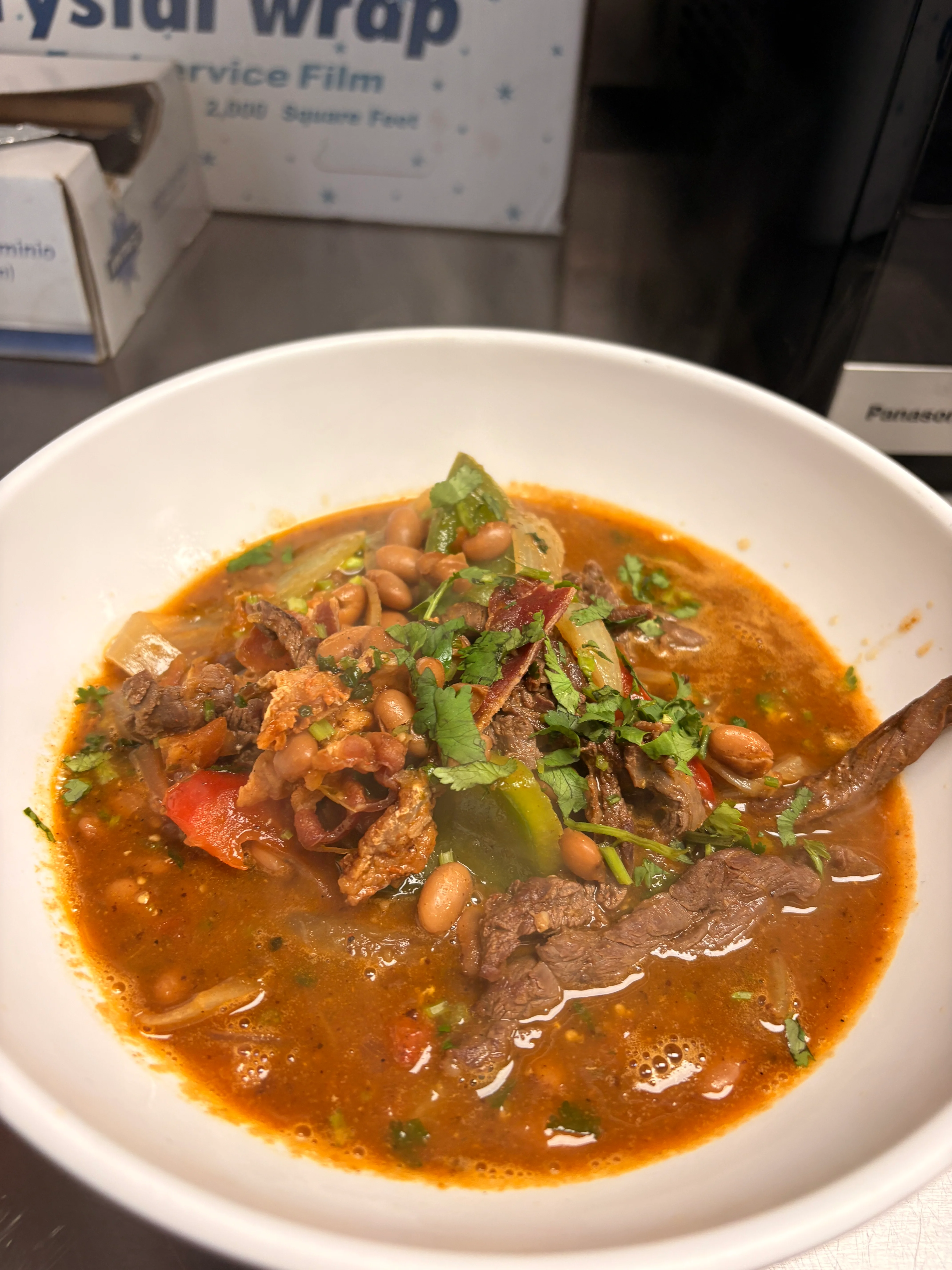 A bowl of hearty soup featuring beef, beans, and vegetables, topped with fresh cilantro.