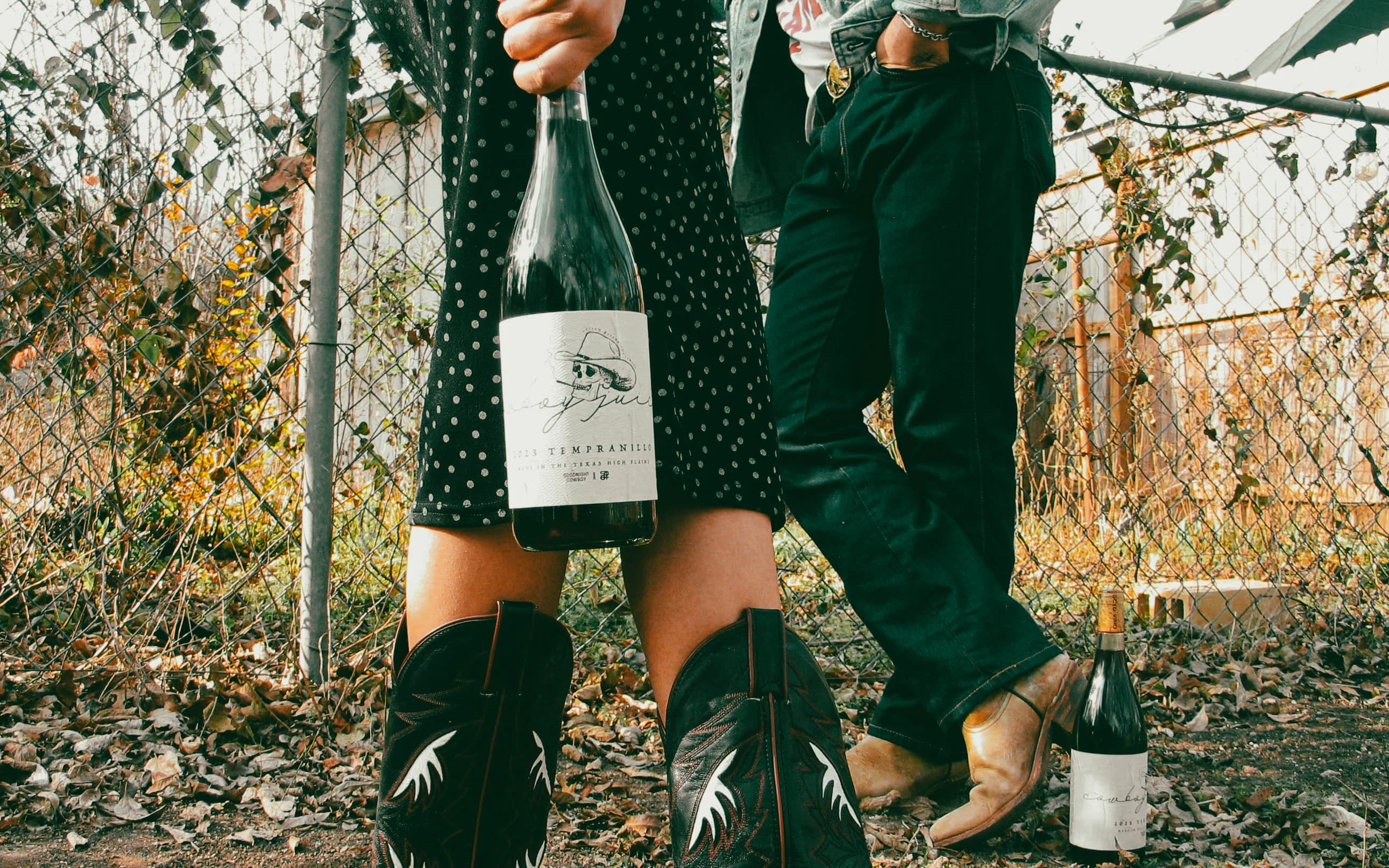 Couple holding wine bottles in a rustic outdoor setting
