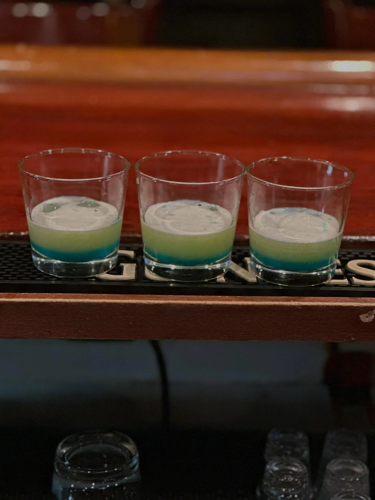 Three colorful shot glasses lined up on a bar, each filled with layered liquids creating a visually striking effect.