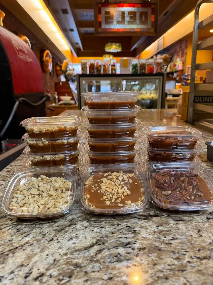 A display of caramel treats in individual containers, featuring various toppings like chopped nuts and caramel sauce, arranged neatly on a countertop.
