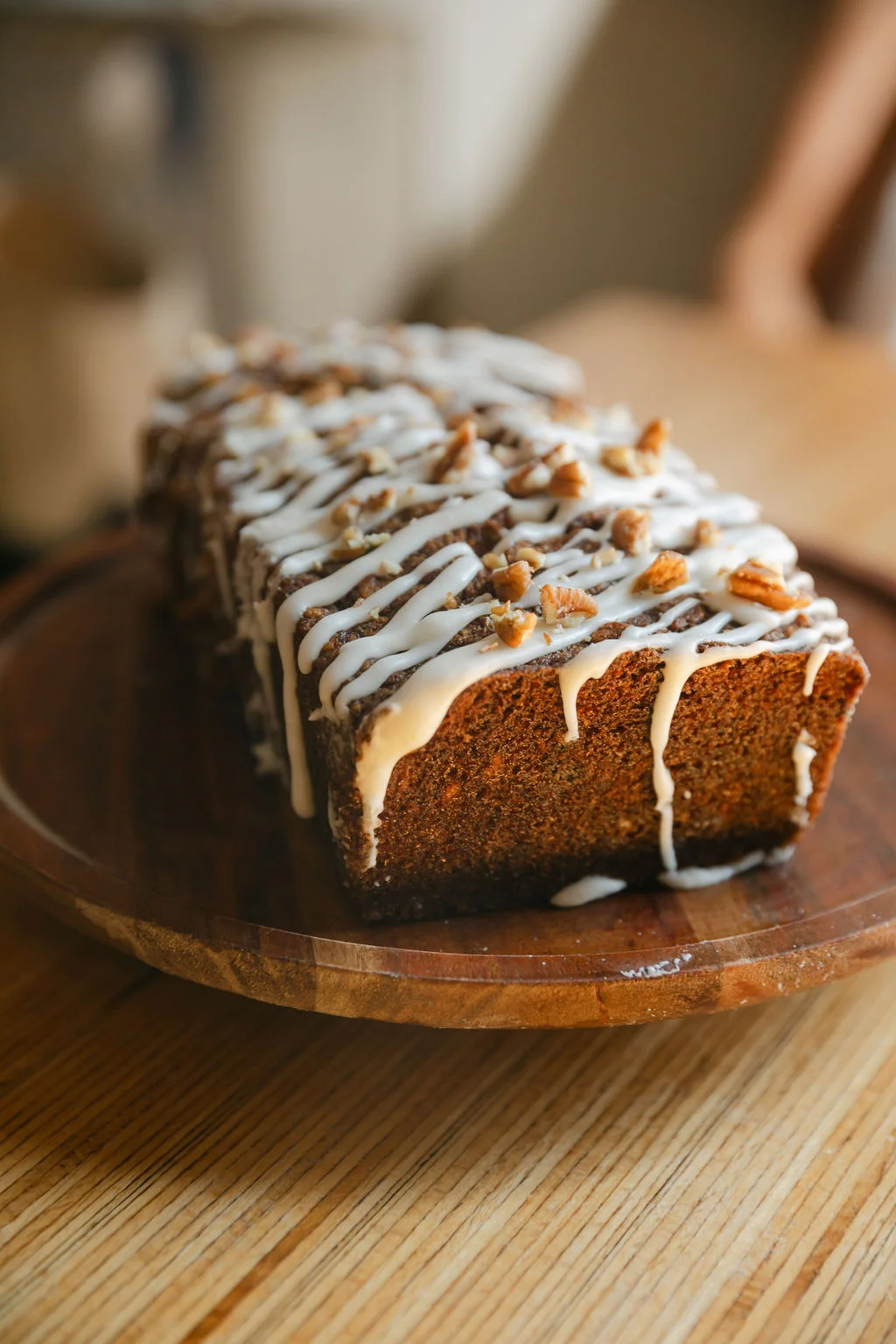 A loaf of cake topped with icing and crumbles, presented on a wooden board.