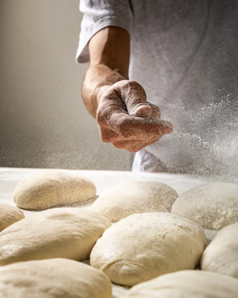 Baker at La Boulangerie & Co in Chicago flouring fresh dough mid-prep using traditional French methods.