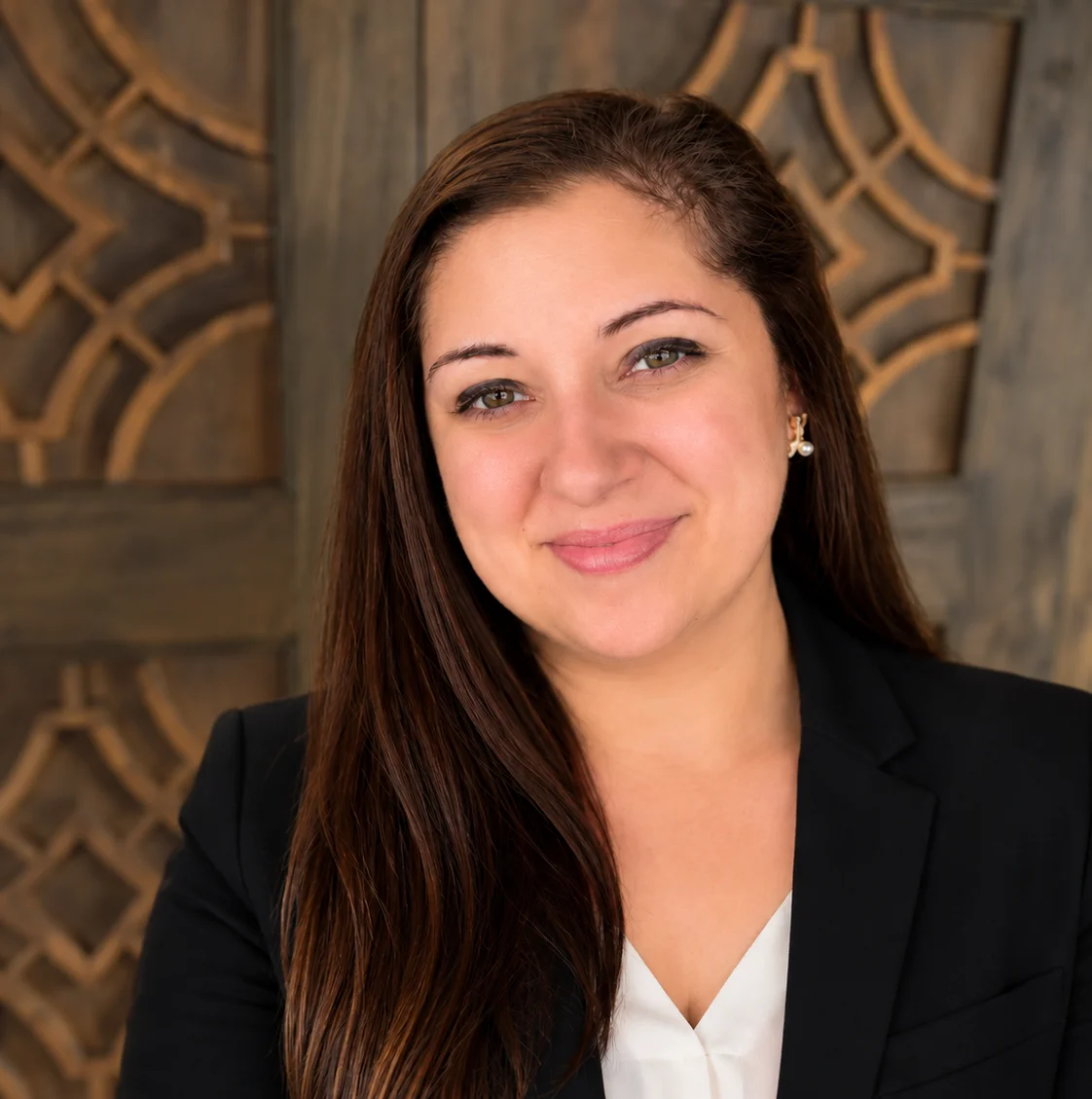 Smiling woman in a black dress against a decorative wooden backdrop