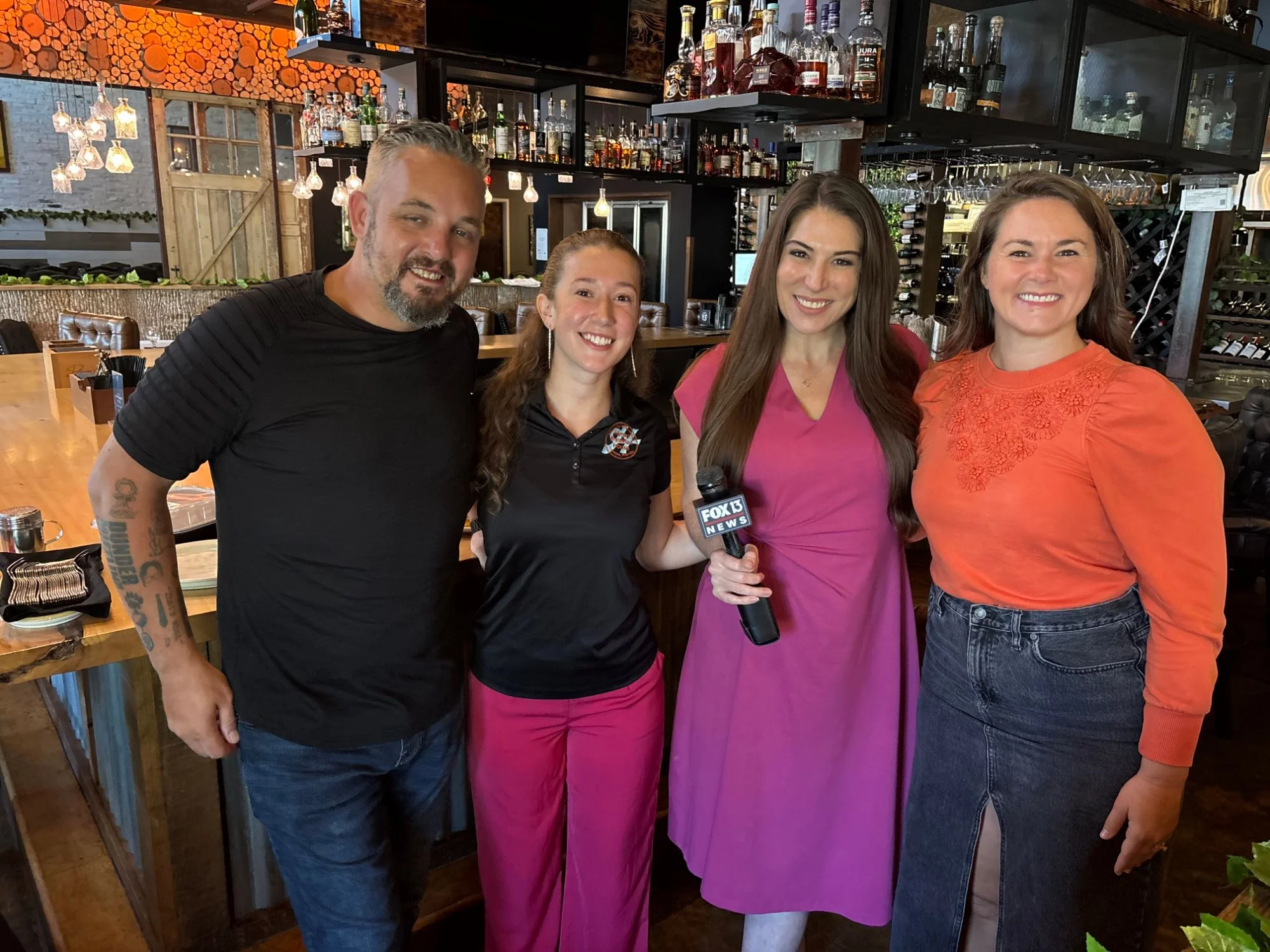 Restaurant team posing with a television reporter inside a stylish bar and dining room
