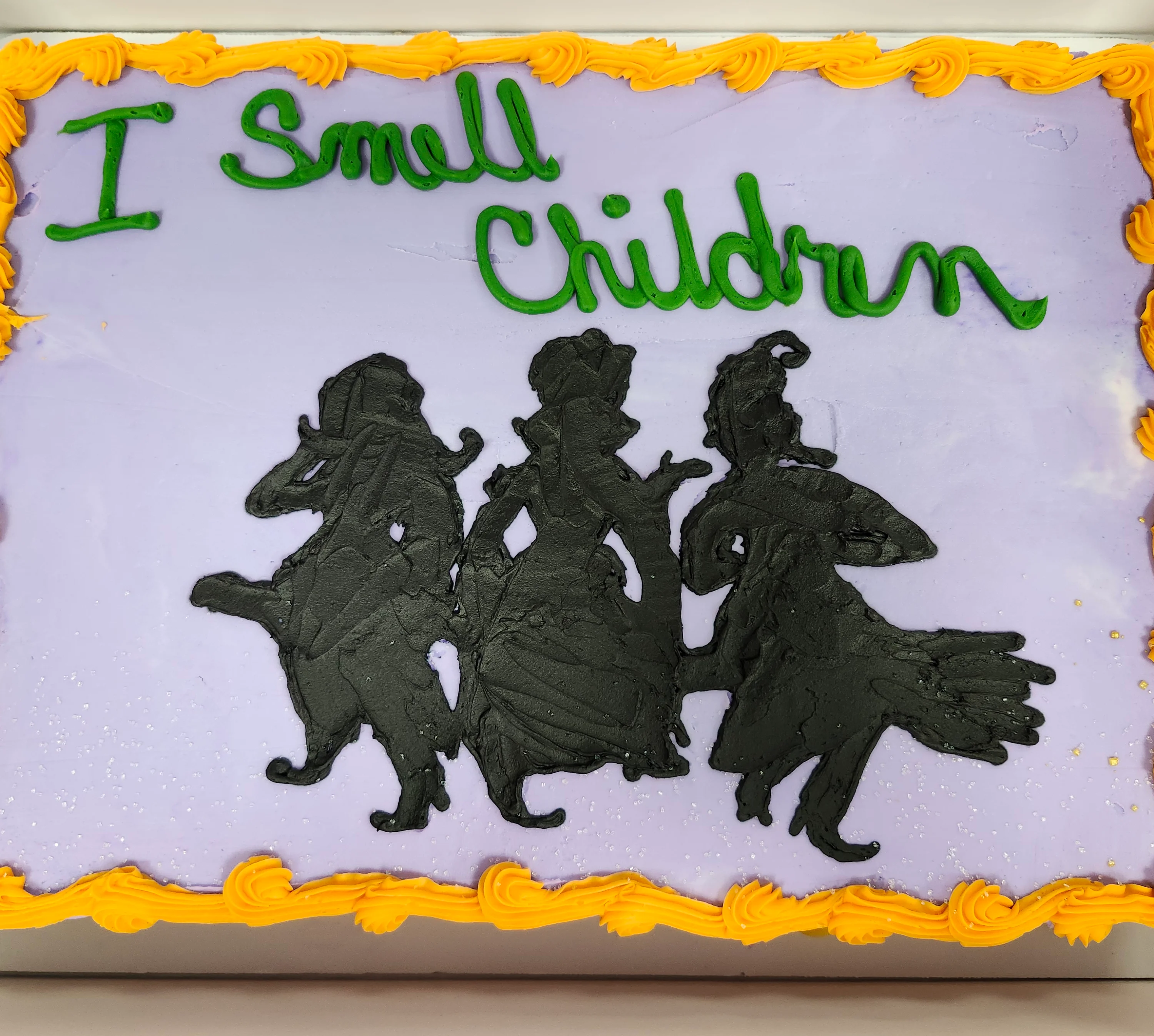 Sheet cake with a pale purple background and golden yellow border and a silhouette of the Sanderson Sisters & "I smell children"