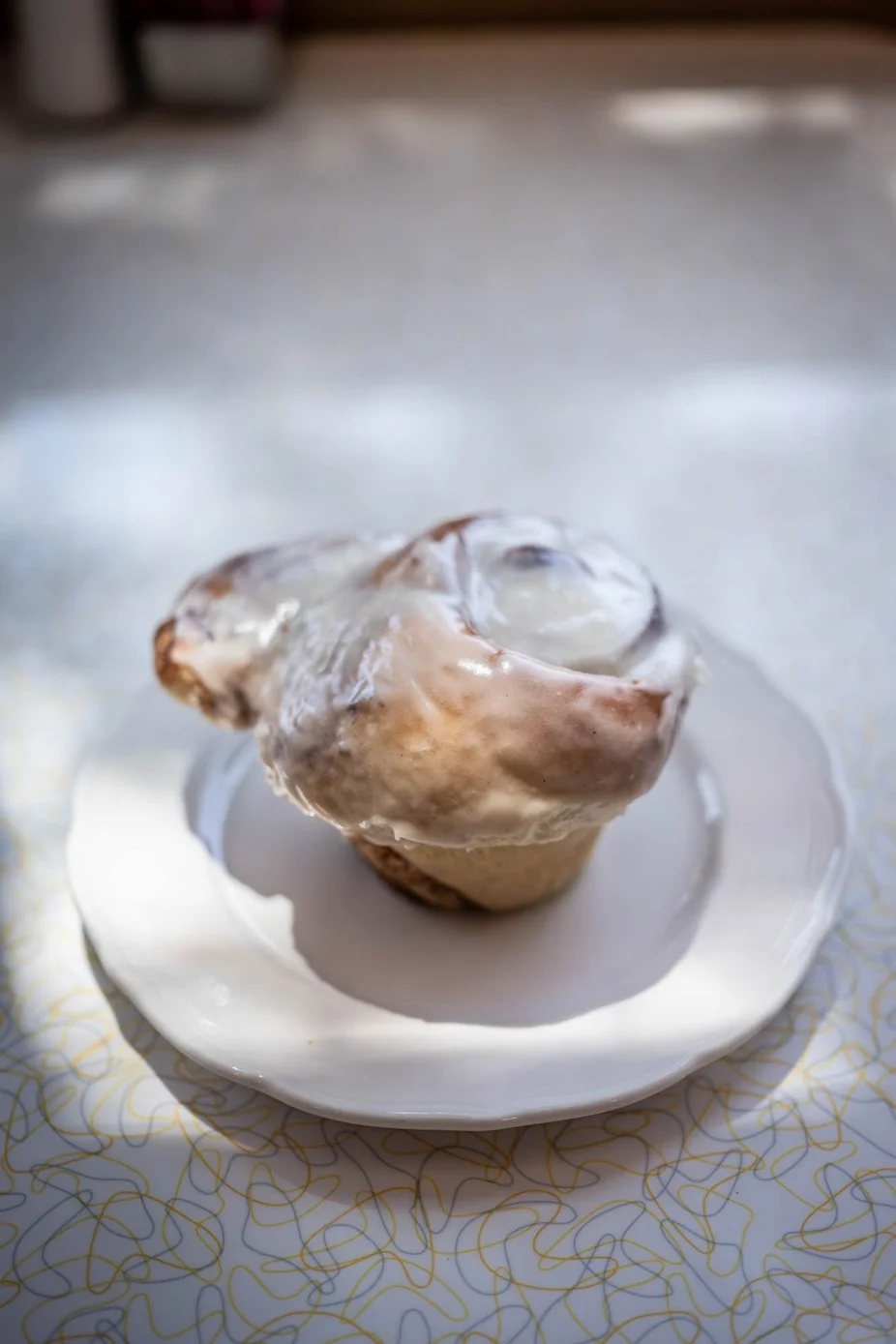 A freshly baked cinnamon roll topped with creamy icing on a white plate.