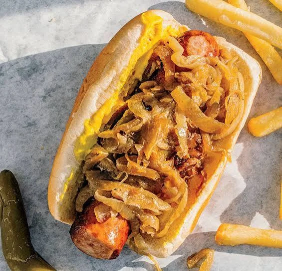 A hot dog topped with sautéed onions and mustard, accompanied by fries on the side.