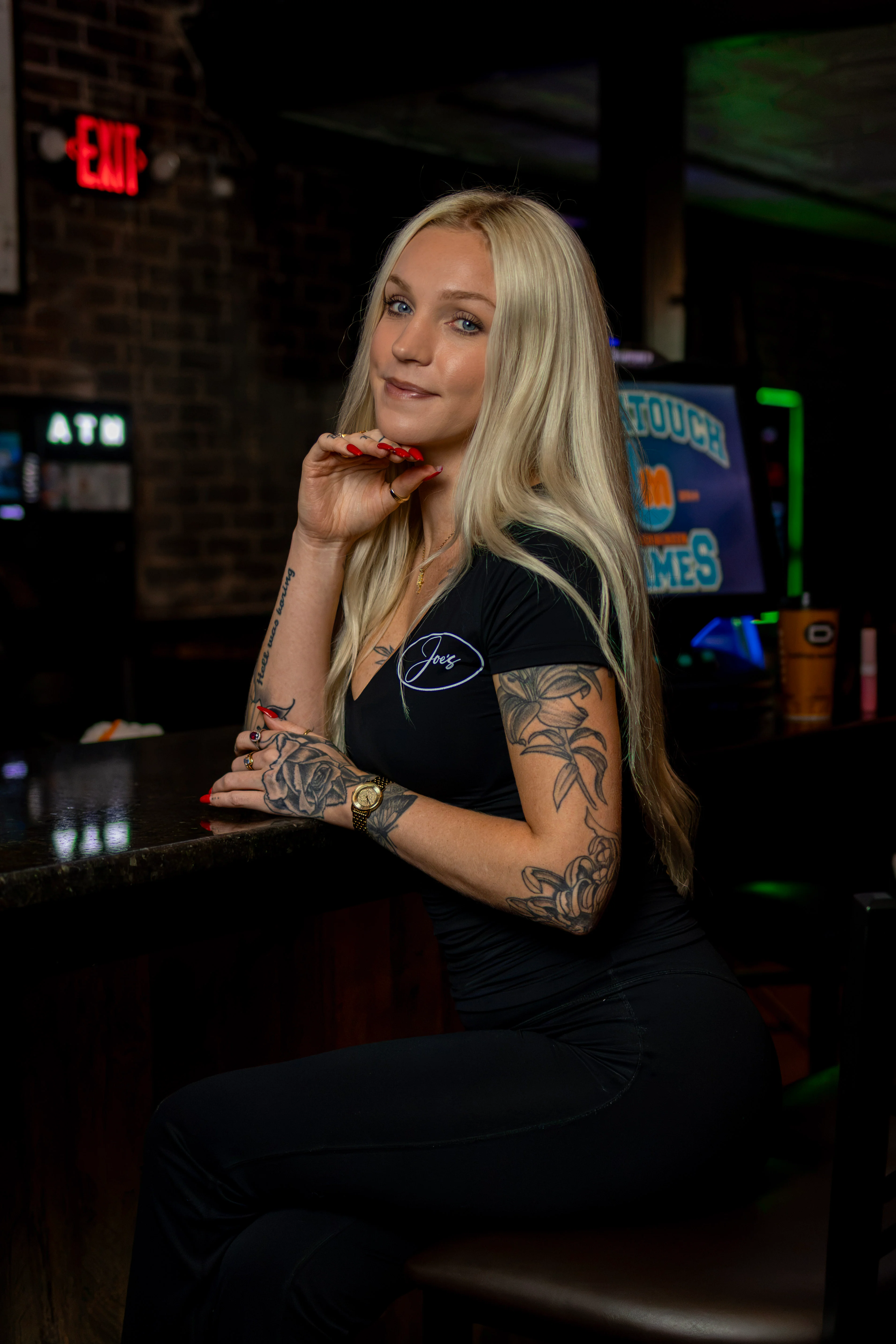 Tattooed bartender posing at a dimly lit restaurant bar