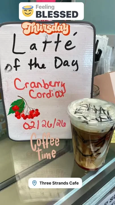 A colorful sign indicating the latte of the day, featuring Cranberry Cordial, along with a prepared drink in a cup.