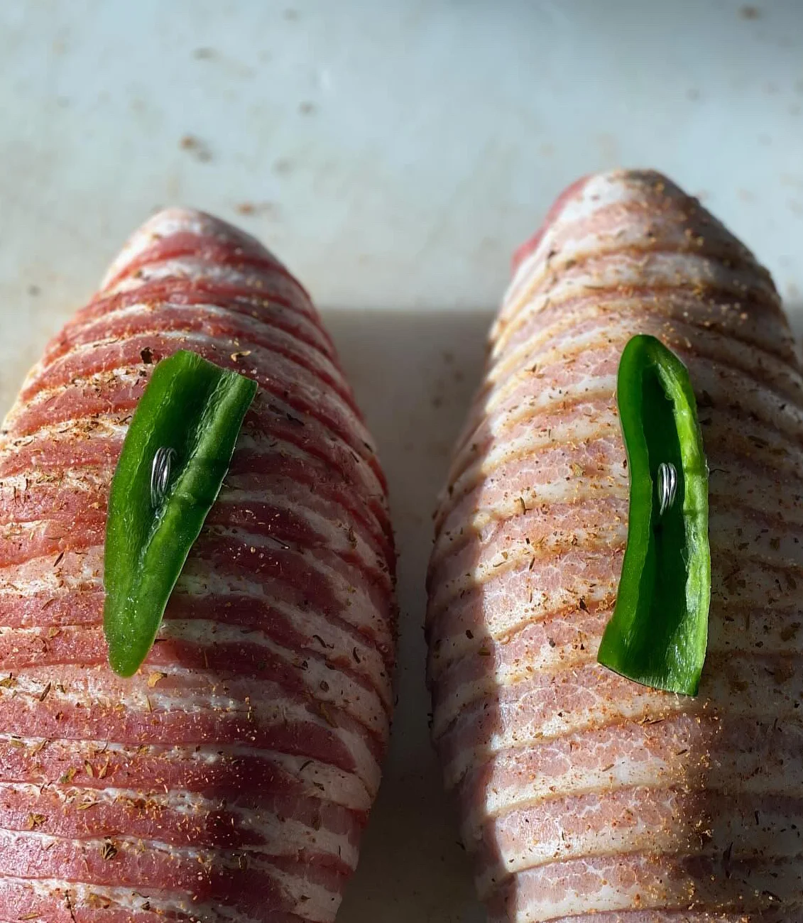 Two bacon-wrapped meatloafs with green pepper garnish on a cutting board.