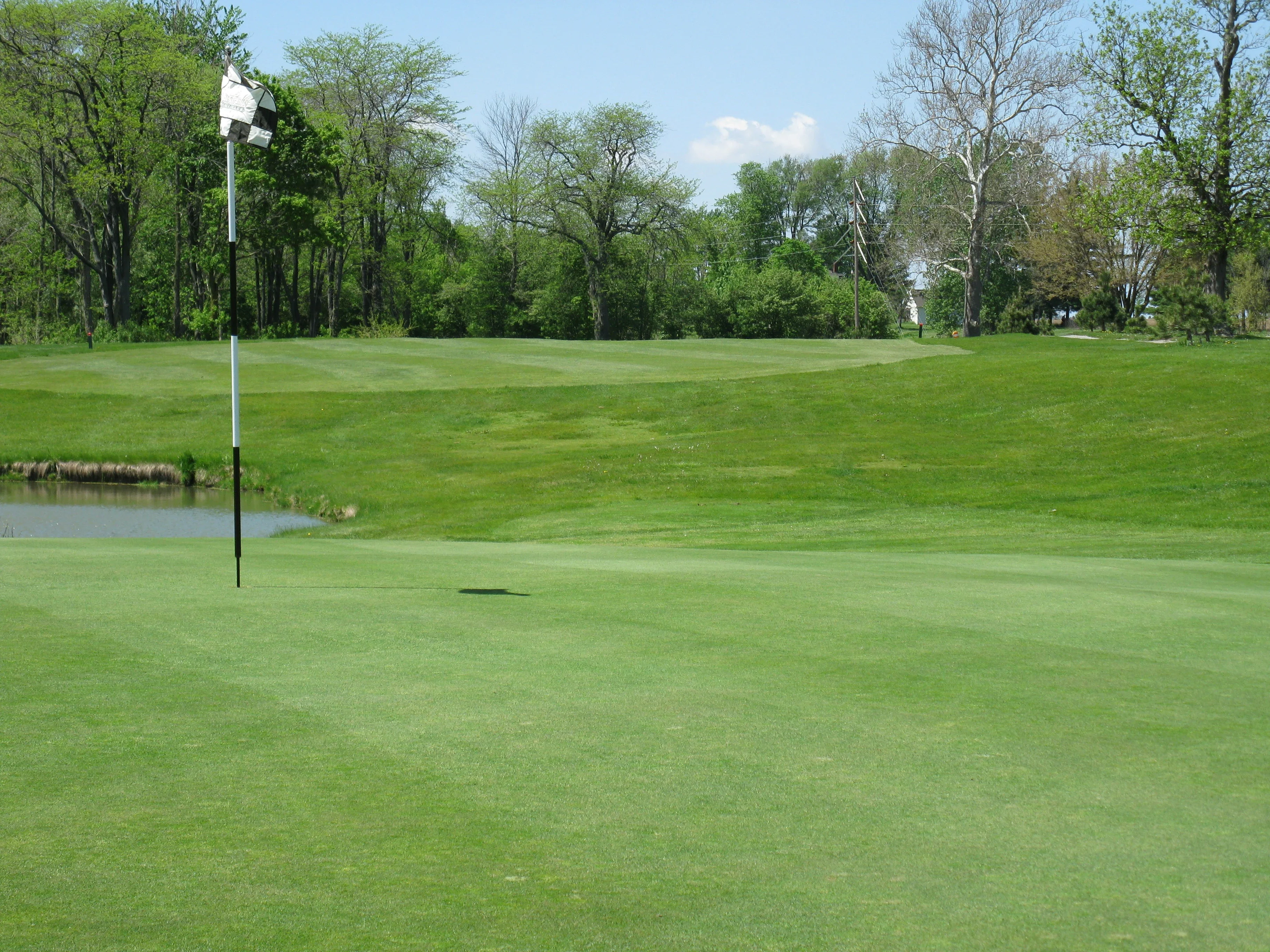 Lush green golf course with a flagstick near a pond