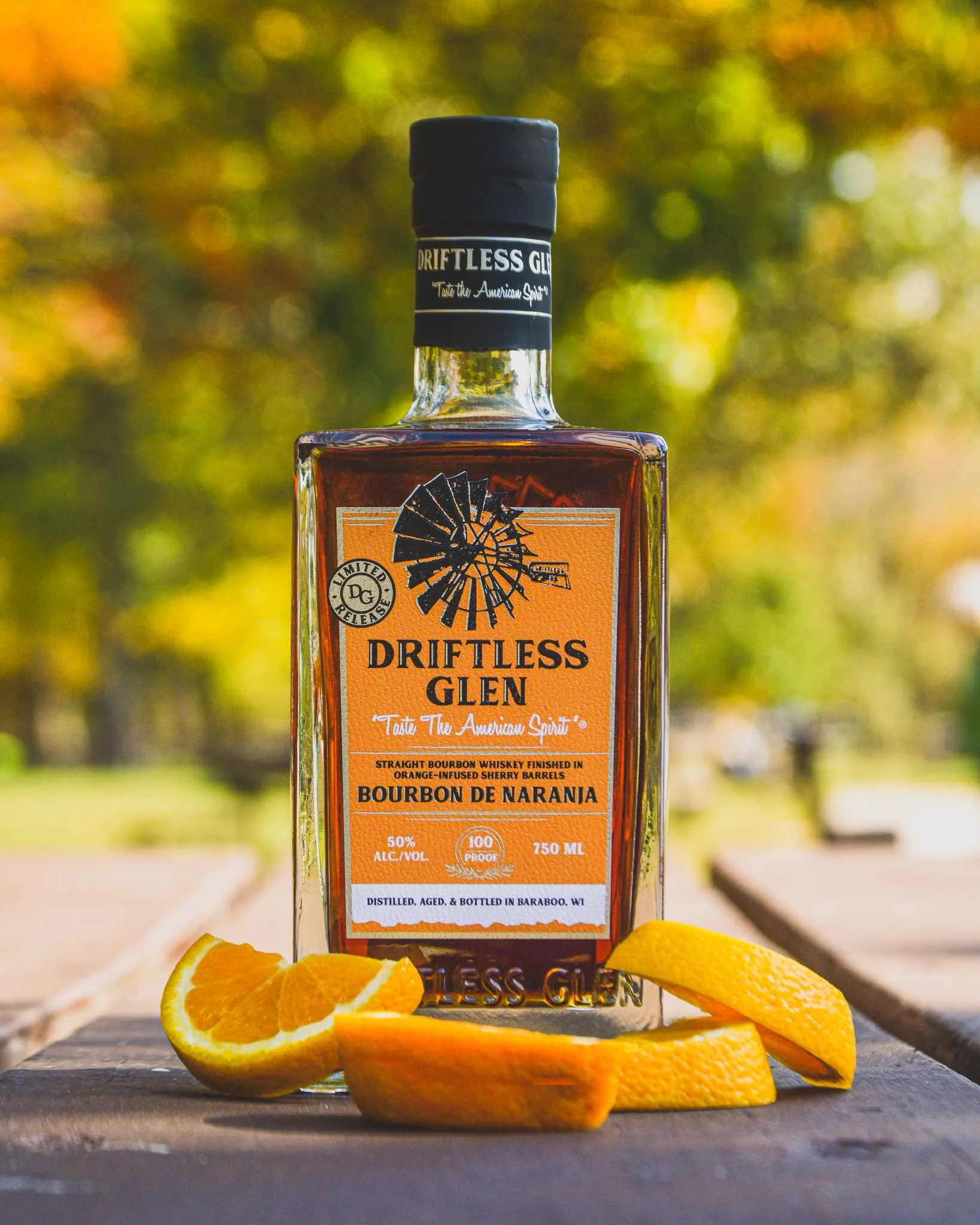 A bottle of Bourbon de Naranja features an orange label and is surrounded by orange slices on a picnic table